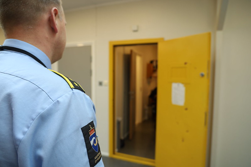 En fengselsansatt står med ryggen til og ser mot en gul dør