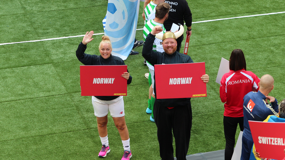 Elisabeth Henriksen står ute på en fotballbane og holder en plakat hvor det står Norway.